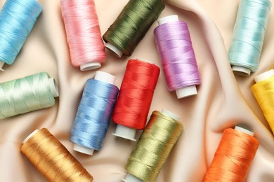 Photo of Spools of sewing threads on beige cloth, top view