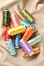 Photo of Spools of sewing threads on beige cloth, top view