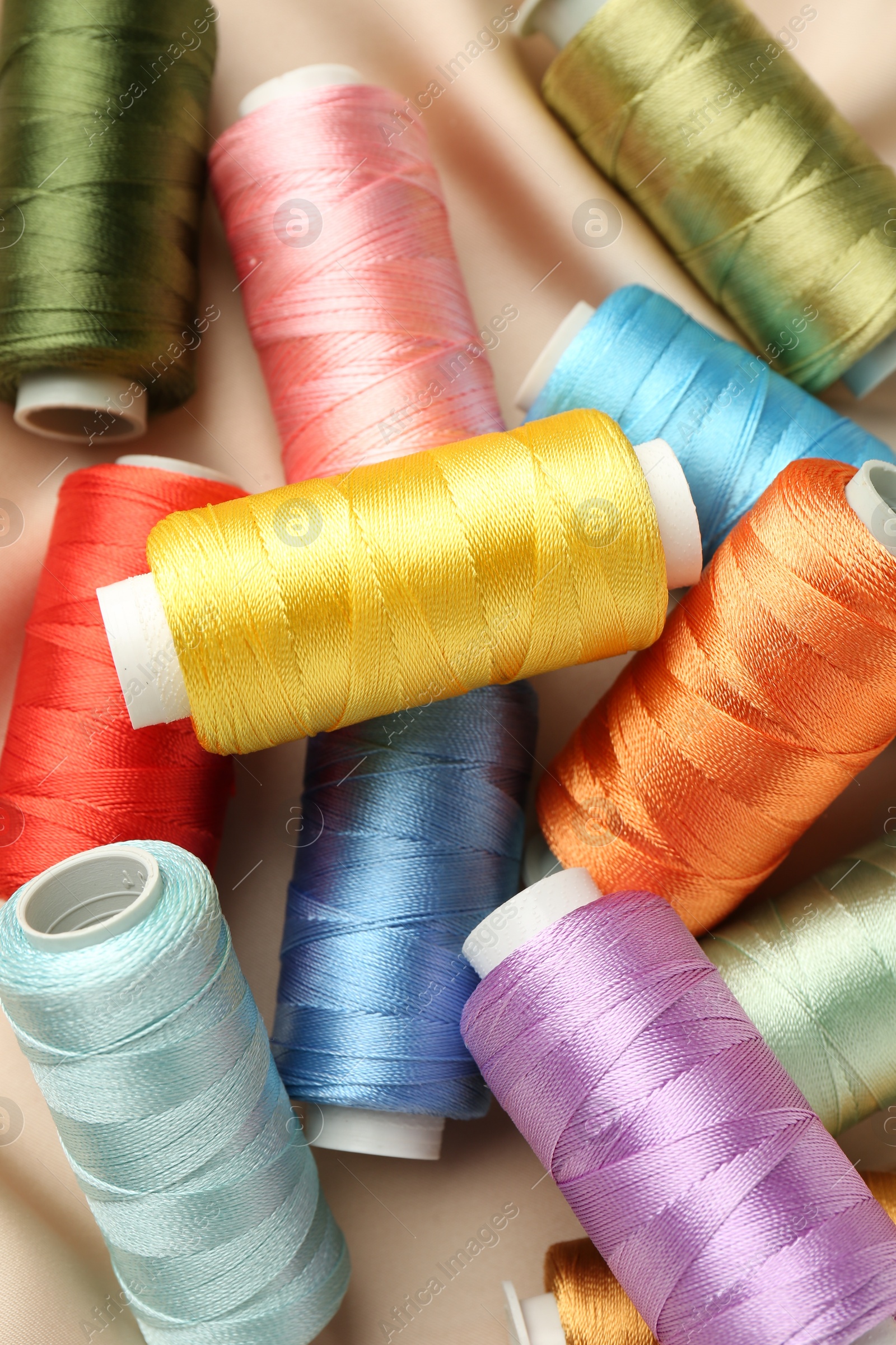 Photo of Spools of sewing threads on beige cloth, top view