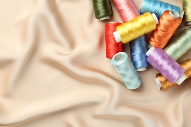 Photo of Spools of sewing threads on beige cloth, top view. Space for text