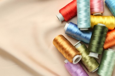 Photo of Spools of sewing threads on beige cloth, top view. Space for text