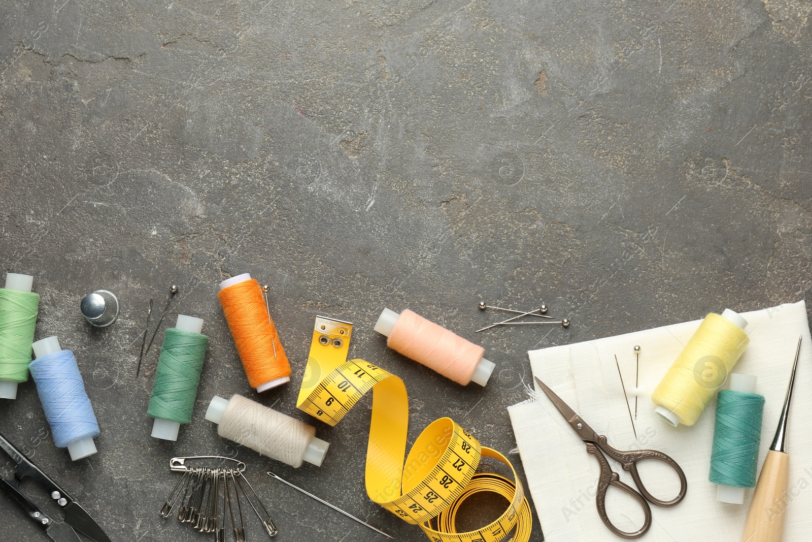 Photo of Flat lay composition with different sewing supplies on grey textured table. Space for text