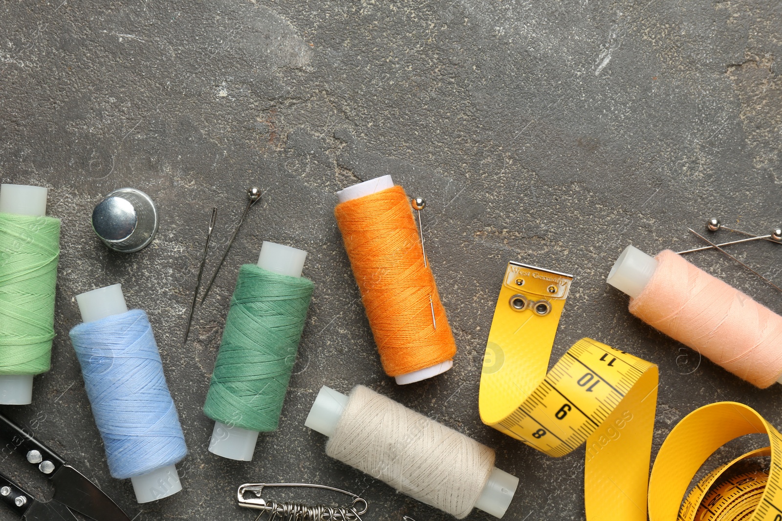 Photo of Flat lay composition with different sewing supplies on grey textured table. Space for text