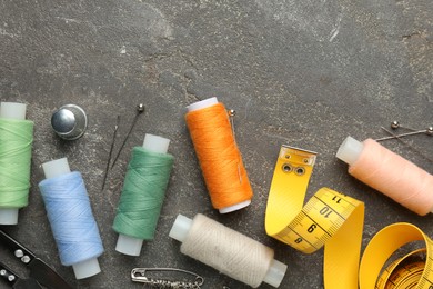 Flat lay composition with different sewing supplies on grey textured table. Space for text