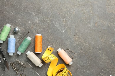 Photo of Flat lay composition with different sewing supplies on grey textured table. Space for text