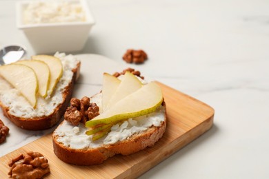 Photo of Delicious ricotta bruschettas with pear and walnut on white marble table, closeup. Space for text