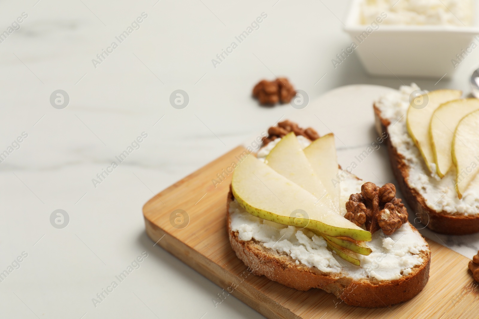 Photo of Delicious ricotta bruschettas with pear and walnut on white marble table, closeup. Space for text