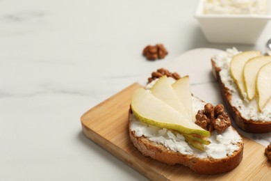 Photo of Delicious ricotta bruschettas with pear and walnut on white marble table, closeup. Space for text