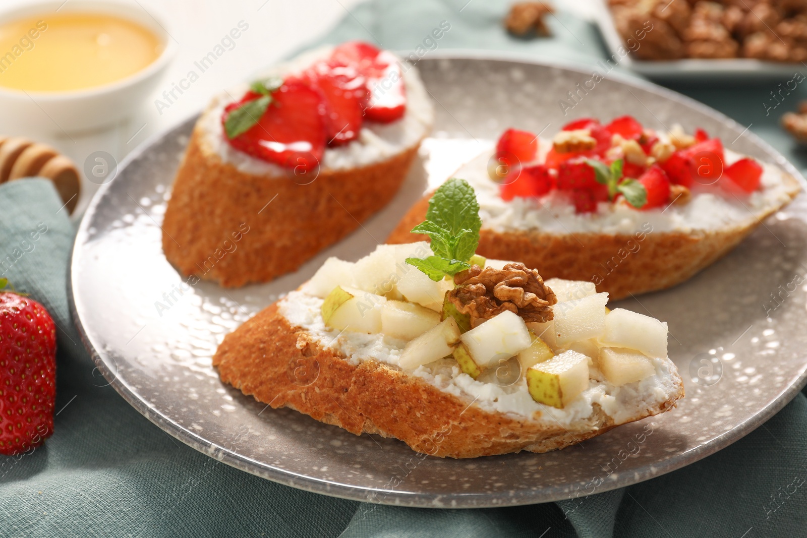 Photo of Delicious ricotta bruschettas with pear, strawberry and walnut on table, closeup