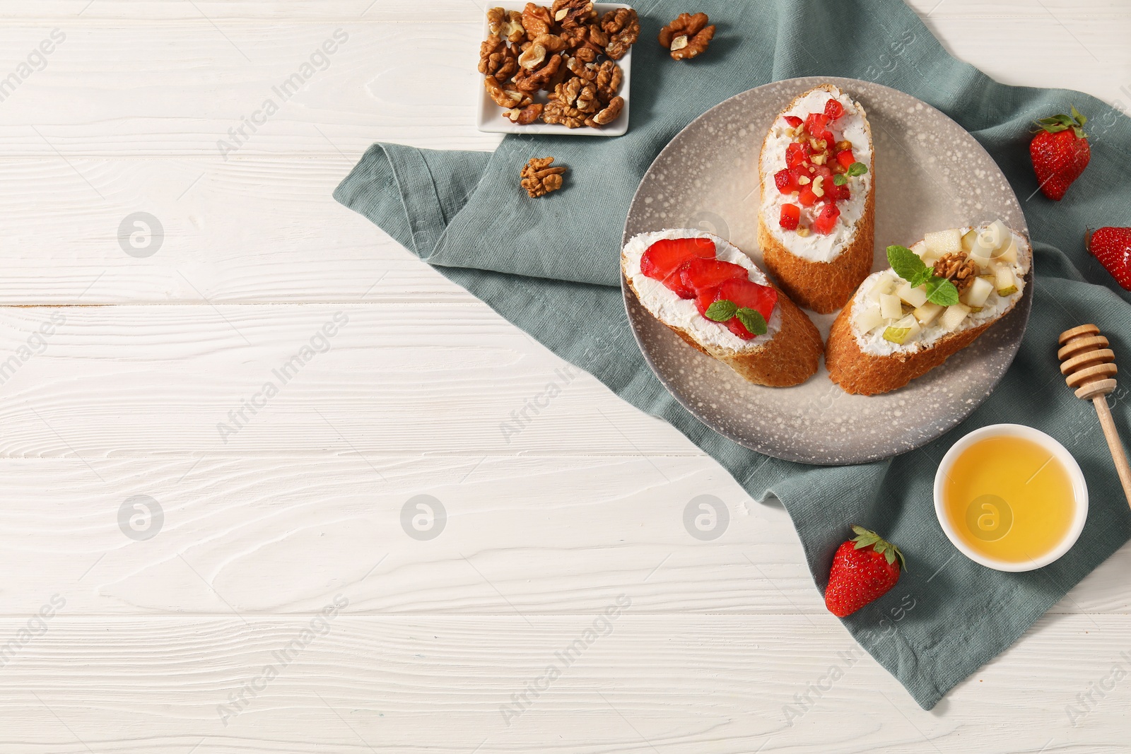 Photo of Delicious ricotta bruschettas with pear, strawberry and walnut on white wooden table, flat lay. Space for text