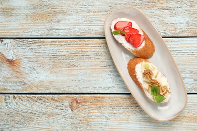 Photo of Delicious ricotta bruschettas with pear, strawberry and walnut on wooden table, top view. Space for text