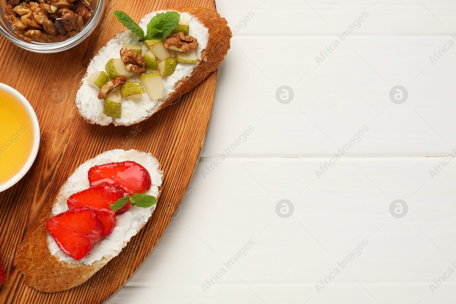 Photo of Delicious ricotta bruschettas with pear, strawberry and walnut on white wooden table, top view. Space for text