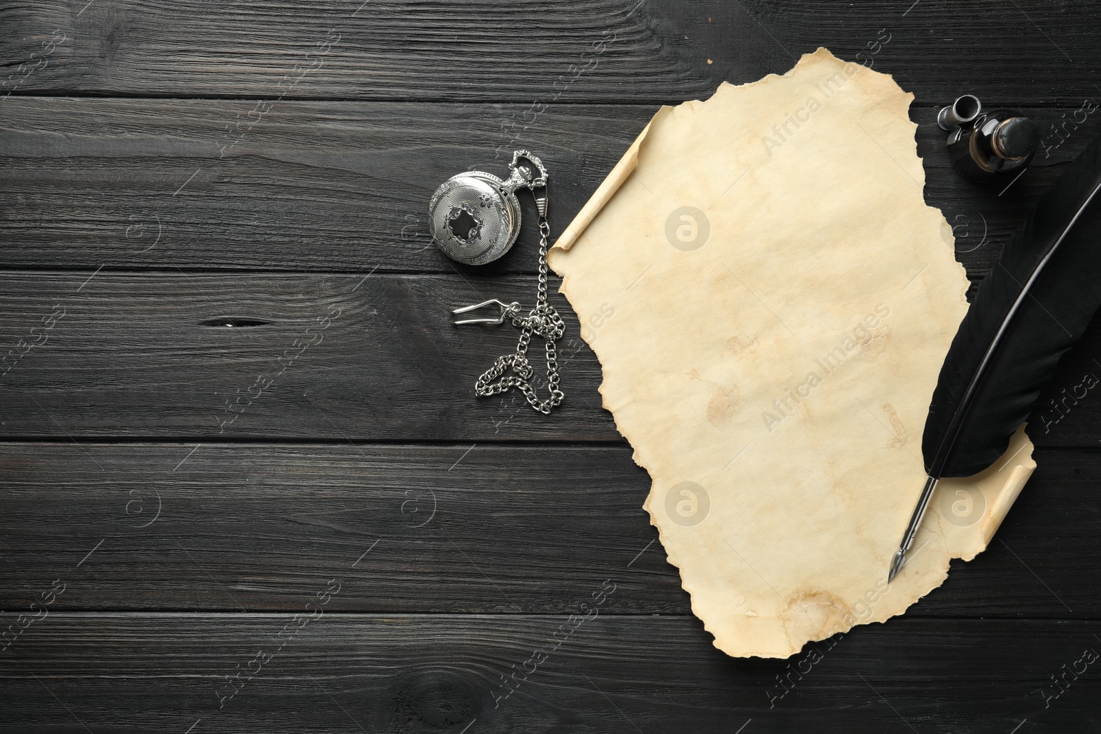 Photo of Sheet of old parchment paper, feather, inkwell and pocket chain clock on black wooden table, top view. Space for text