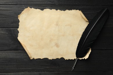 Photo of Sheet of old parchment paper and feather on black wooden table, top view
