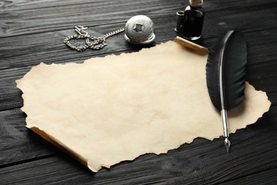 Photo of Sheet of old parchment paper, feather, inkwell and pocket chain clock on black wooden table
