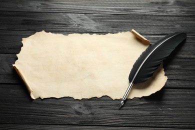 Photo of Sheet of old parchment paper and feather on black wooden table