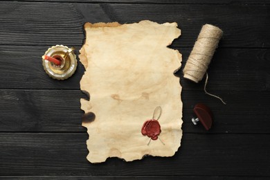 Photo of Sheet of old parchment paper with wax stamp, twine and candle on black wooden table, top view