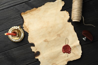 Photo of Sheet of old parchment paper with wax stamp, twine and candle on black wooden table, top view