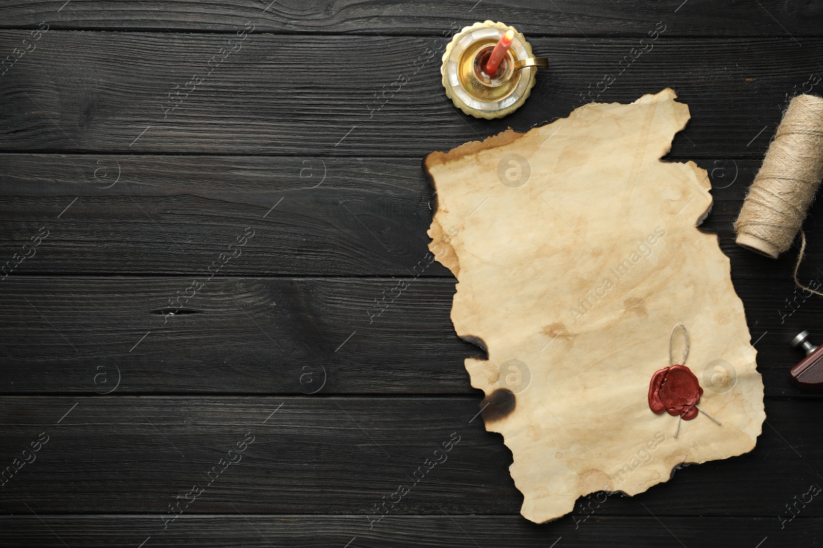 Photo of Sheet of old parchment paper with wax stamp, twine and candle on black wooden table, top view. Space for text