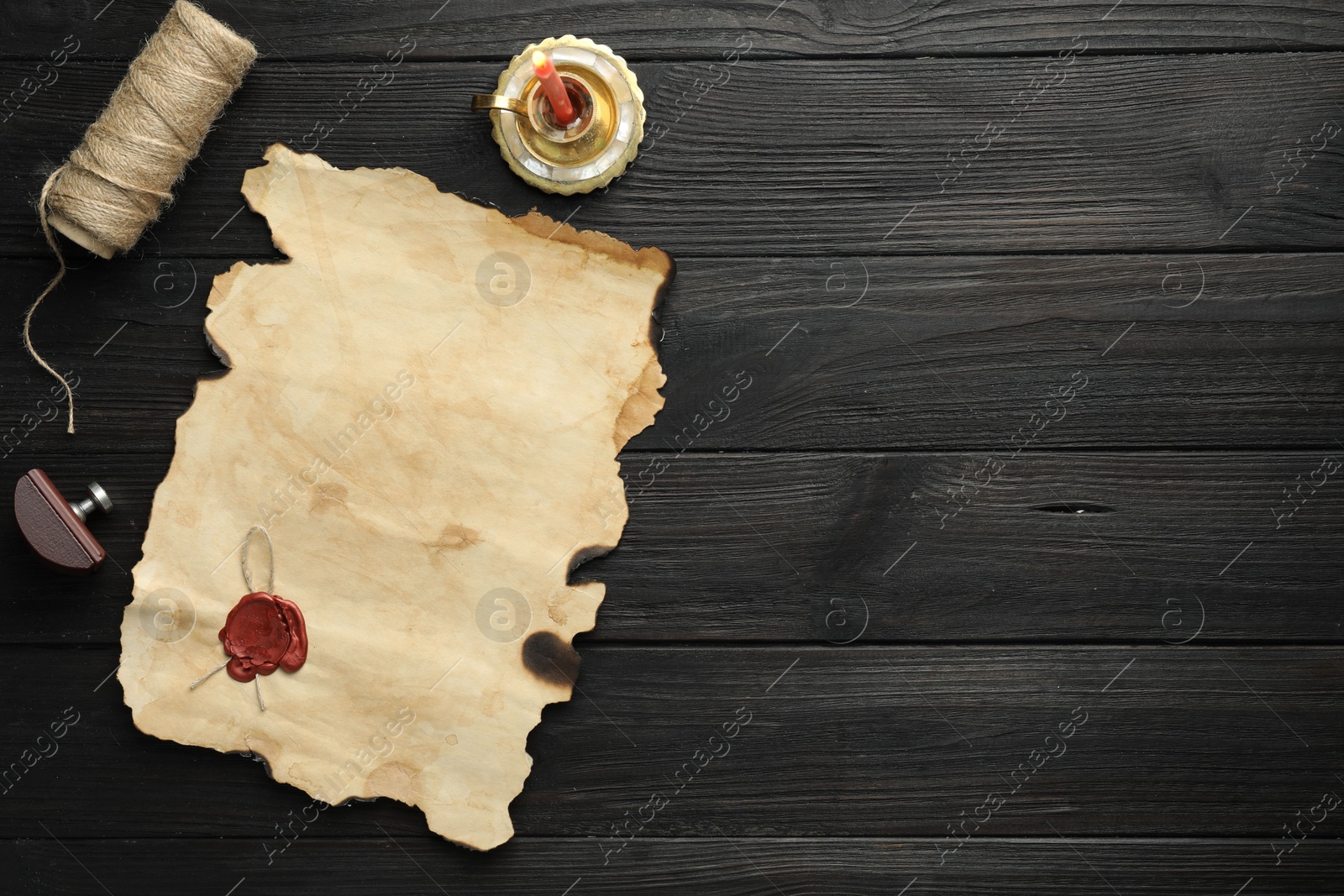 Photo of Sheet of old parchment paper with wax stamp, twine and candle on black wooden table, top view. Space for text