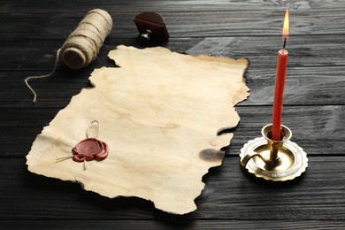 Sheet of old parchment paper with wax stamp, twine and candle on black wooden table