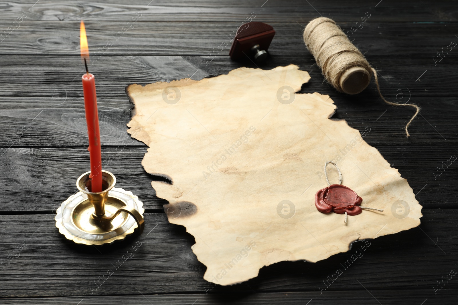 Photo of Sheet of old parchment paper with wax stamp, twine and candle on black wooden table