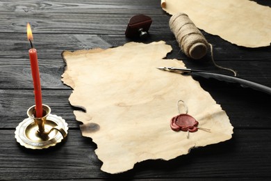 Photo of Sheet of old parchment paper with wax stamp, twine and candle on black wooden table