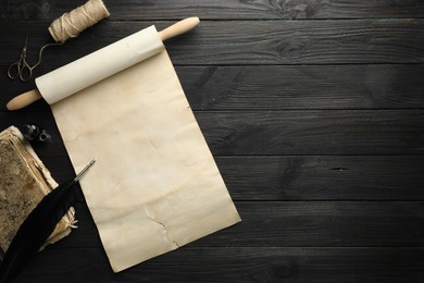 Sheet of old parchment paper, inkwell, scissors, vintage book, feather and twine on black wooden table, top view. Space for text