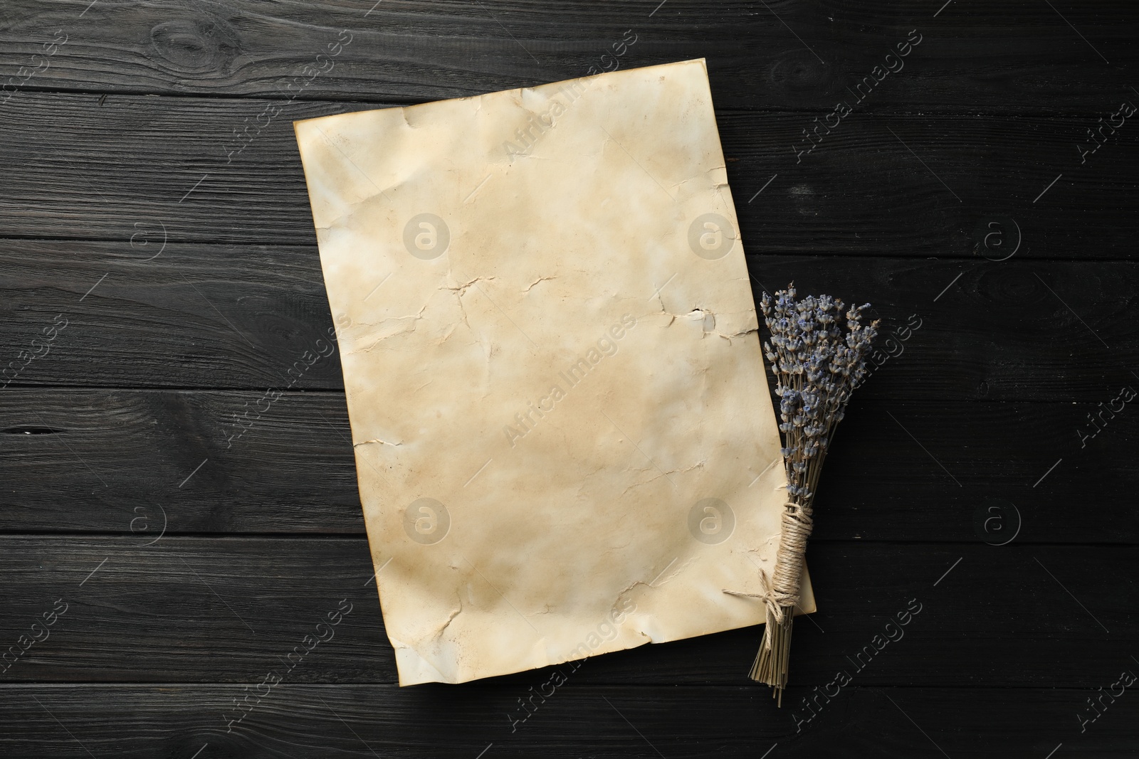 Photo of Sheet of old parchment paper and lavender flowers on black wooden table, top view