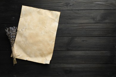 Photo of Sheet of old parchment paper and lavender flowers on black wooden table, top view. Space for text