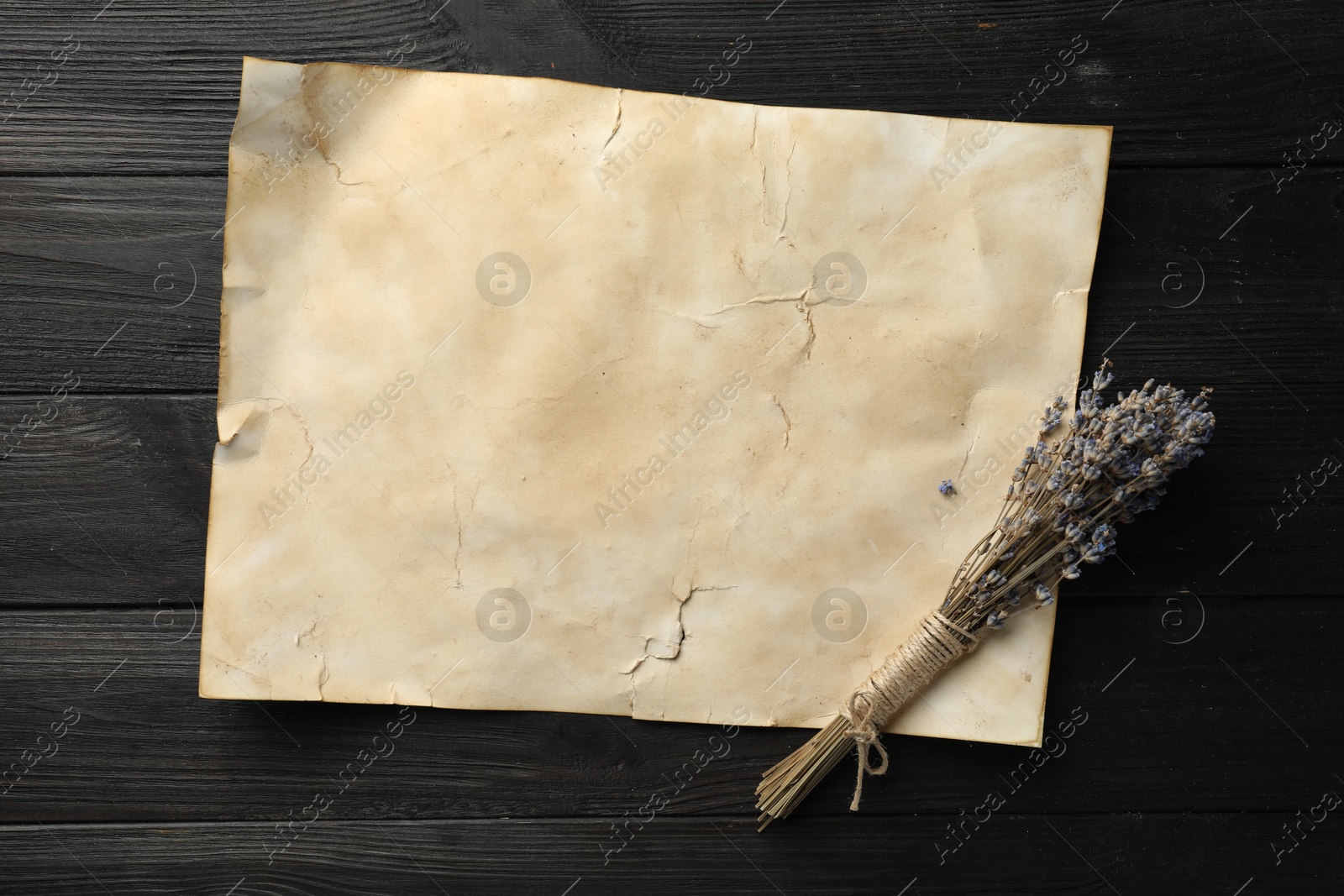 Photo of Sheet of old parchment paper and lavender flowers on black wooden table, top view