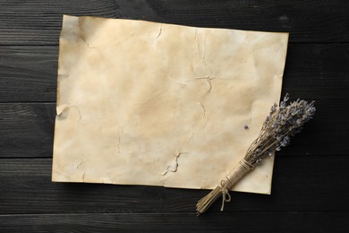 Sheet of old parchment paper and lavender flowers on black wooden table, top view