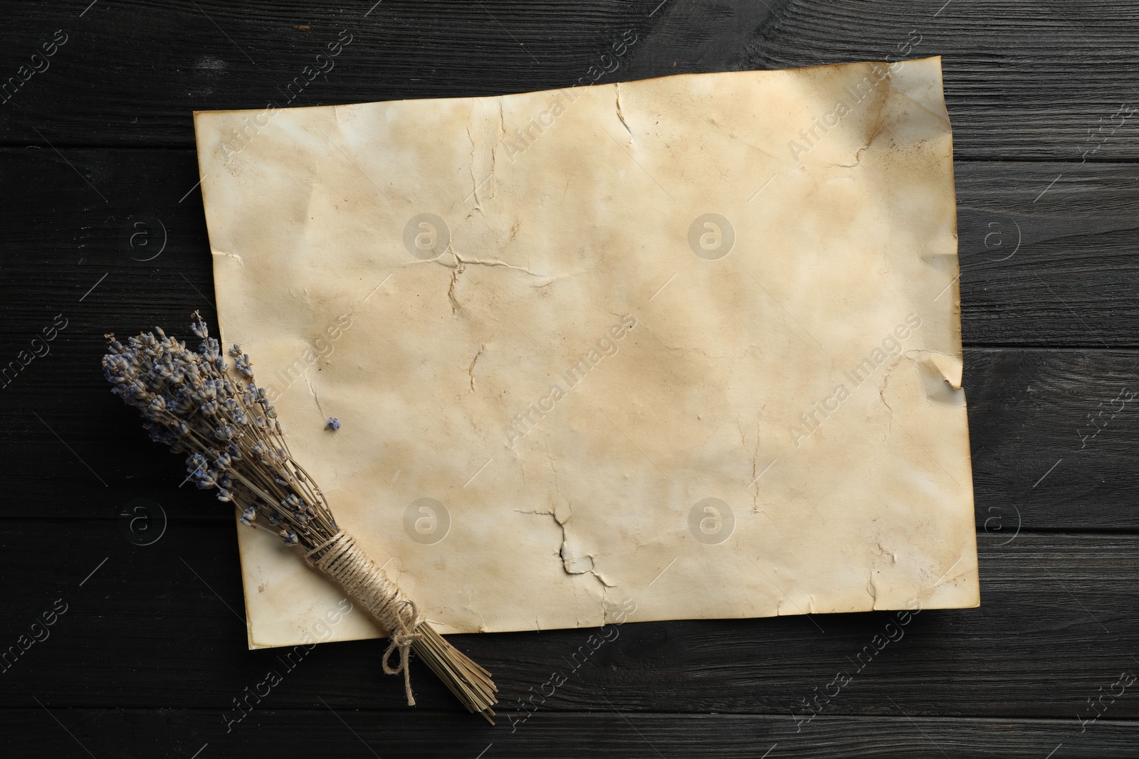 Photo of Sheet of old parchment paper and lavender flowers on black wooden table, top view