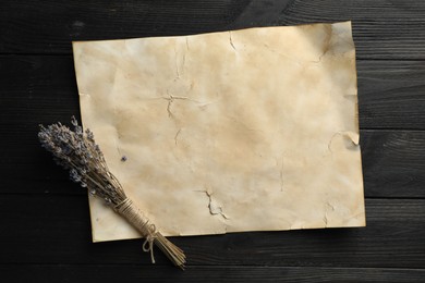 Sheet of old parchment paper and lavender flowers on black wooden table, top view