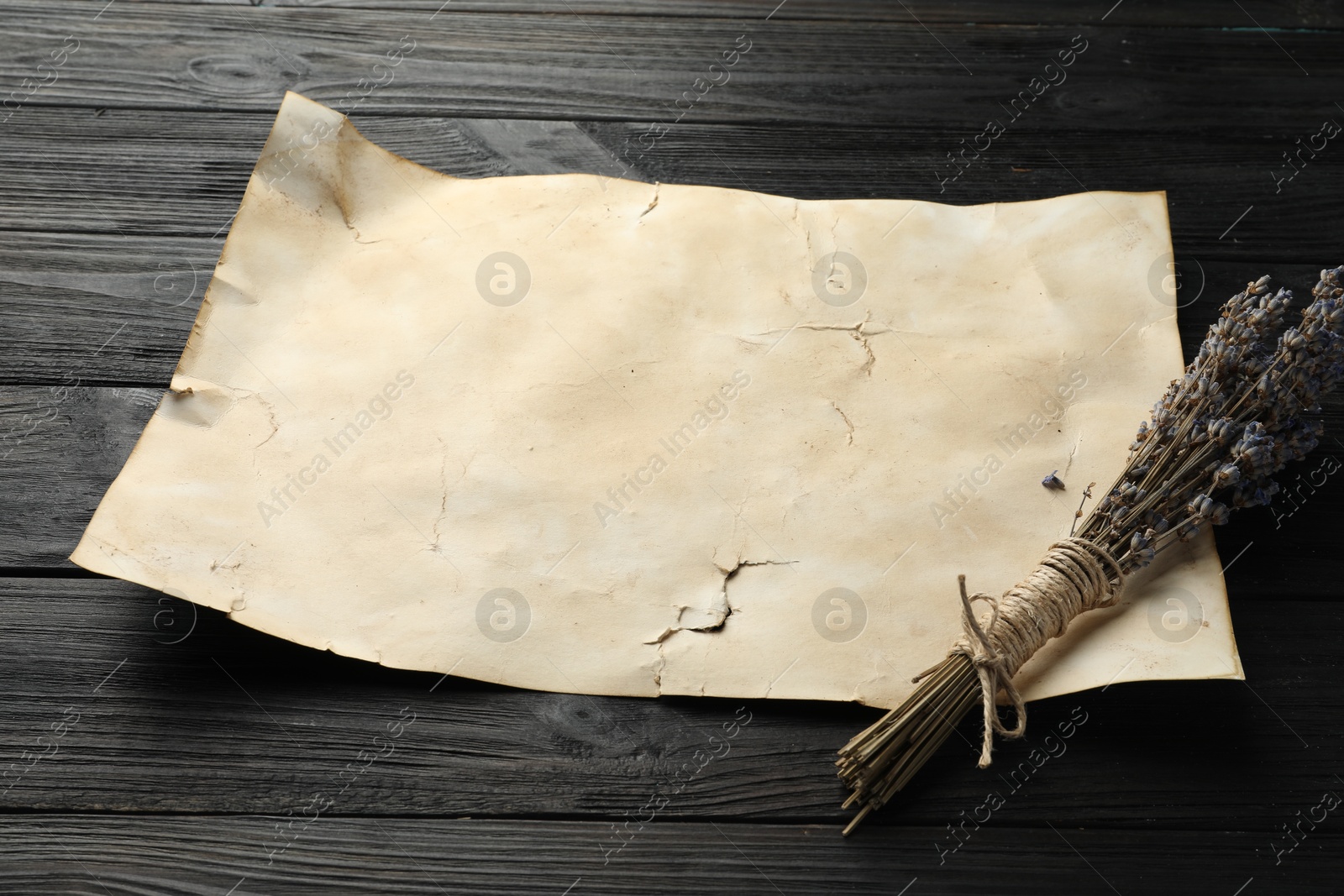 Photo of Sheet of old parchment paper and lavender flowers on black wooden table