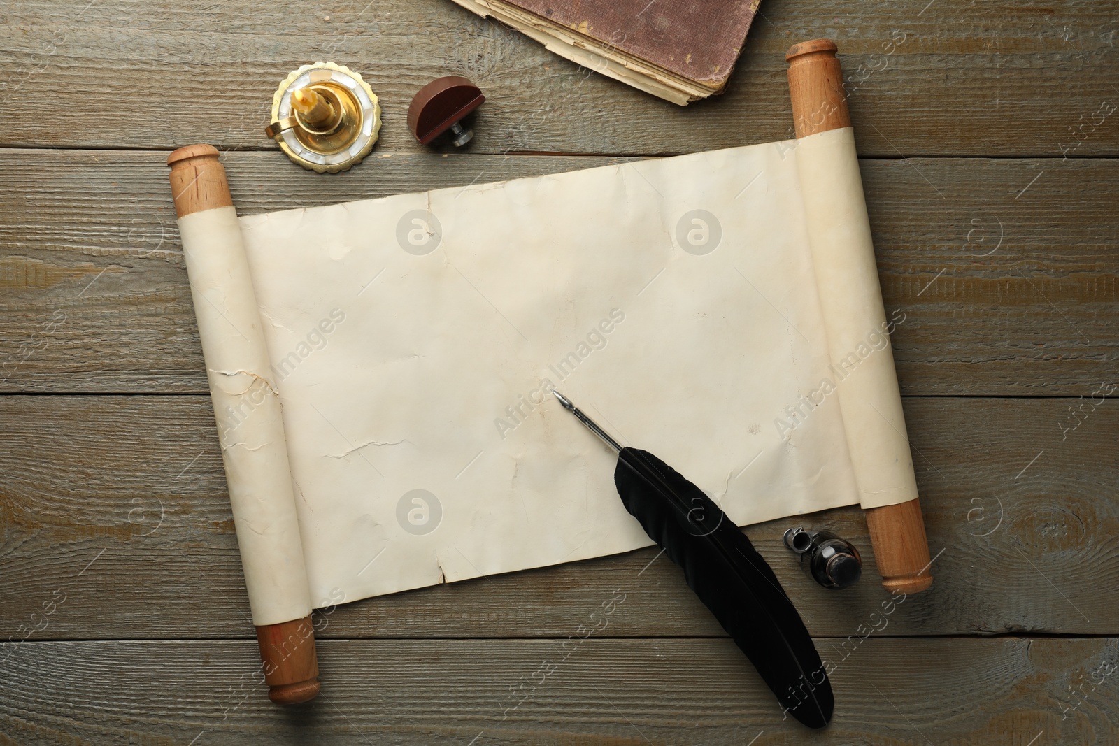 Photo of Sheet of old parchment paper, wax stamp, feather, inkwell, candle and vintage book on wooden table, top view