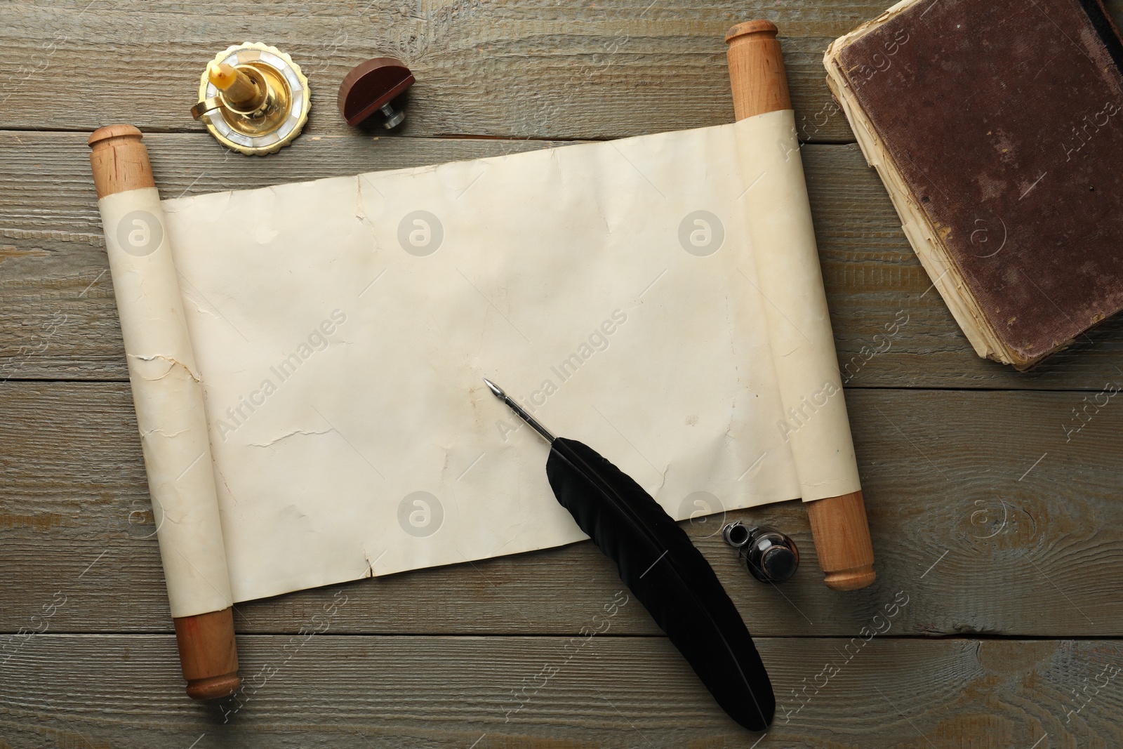 Photo of Sheet of old parchment paper, wax stamp, feather, inkwell, candle and vintage book on wooden table, top view