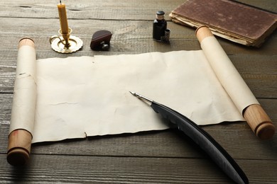 Sheet of old parchment paper, wax stamp, black feather, inkwell, candle and vintage book on wooden table