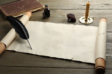 Photo of Sheet of old parchment paper, wax stamp, black feather, inkwell, candle and vintage book on wooden table