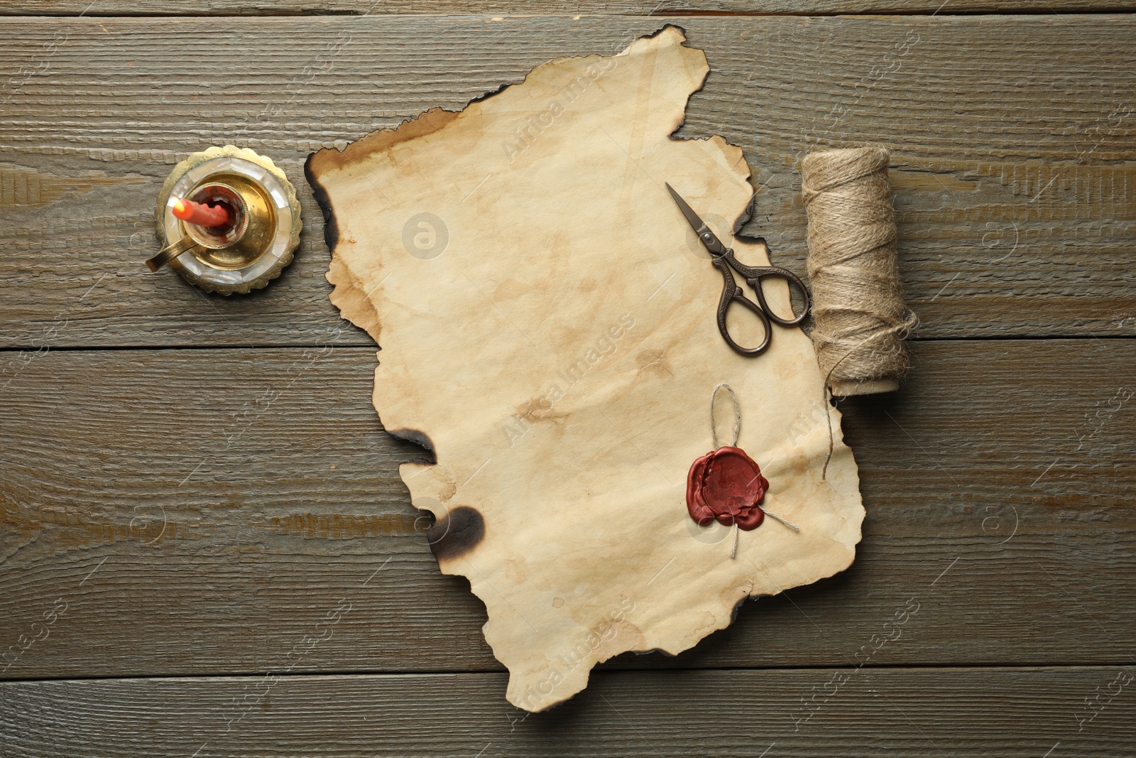 Photo of Sheet of old parchment paper with wax stamp, scissors, twine and candle on wooden table, top view