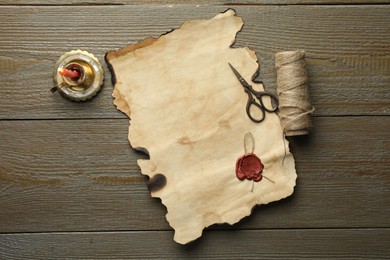 Photo of Sheet of old parchment paper with wax stamp, scissors, twine and candle on wooden table, top view