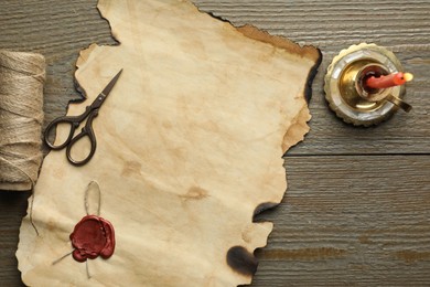 Sheet of old parchment paper with wax stamp, scissors, twine and candle on wooden table, top view