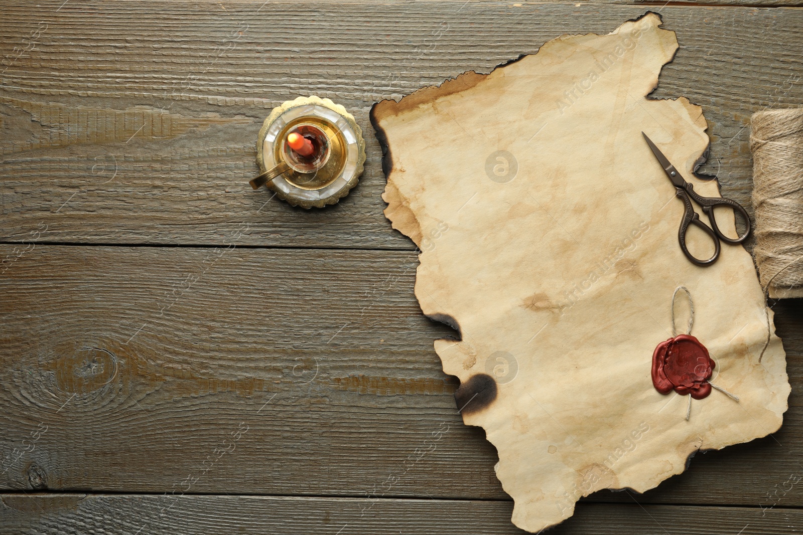 Photo of Sheet of old parchment paper with wax stamp, scissors, twine and candle on wooden table, top view. Space for text