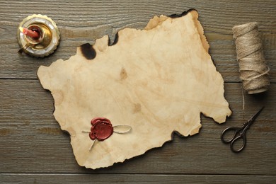 Sheet of old parchment paper with wax stamp, scissors, twine and candle on wooden table, top view