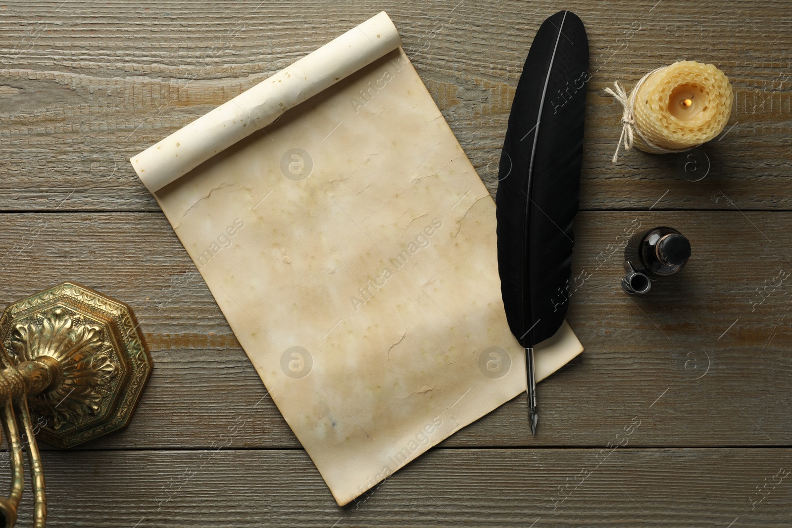 Photo of Sheet of old parchment paper, black feather, inkwell and candle on wooden table, top view