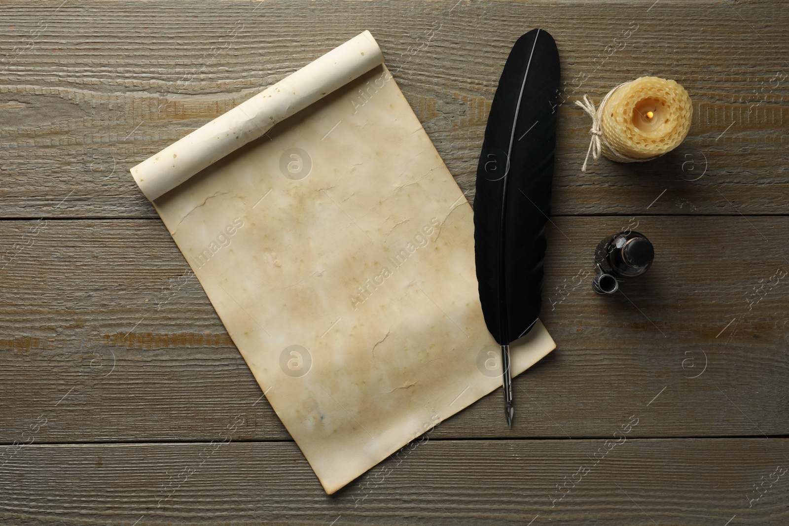 Photo of Sheet of old parchment paper, black feather, inkwell and candle on wooden table, top view