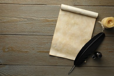 Photo of Sheet of old parchment paper, black feather, inkwell and candle on wooden table, top view. Space for text