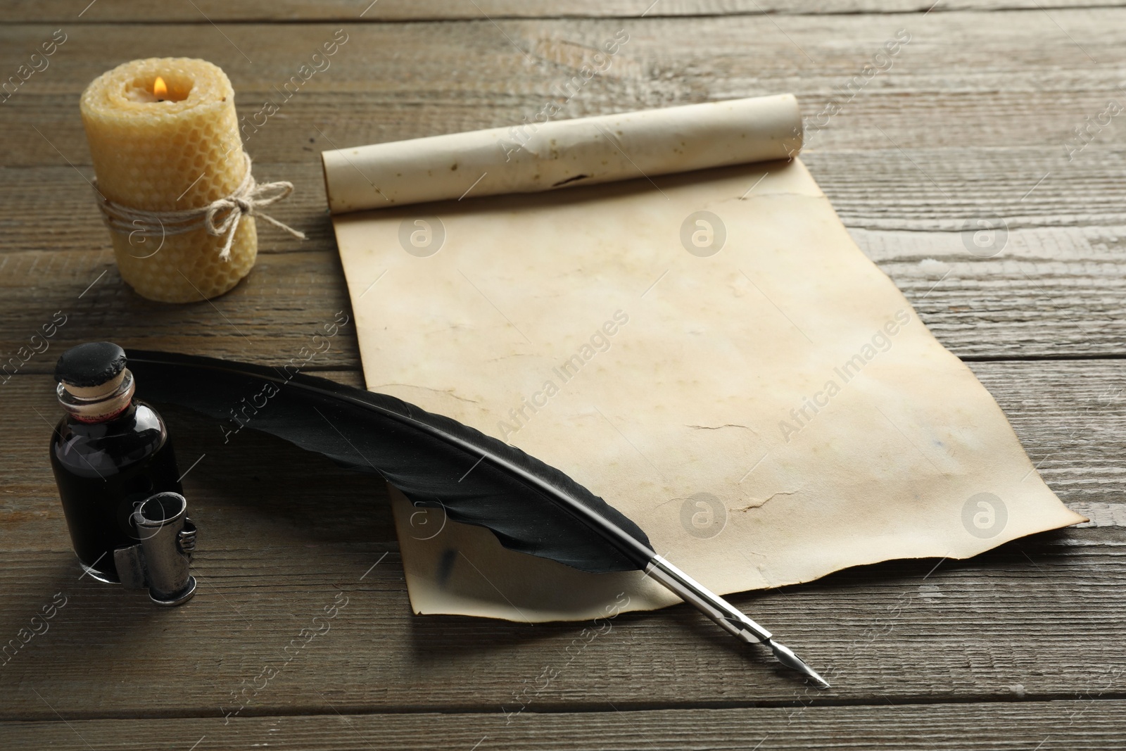 Photo of Sheet of old parchment paper, black feather, inkwell and candle on wooden table