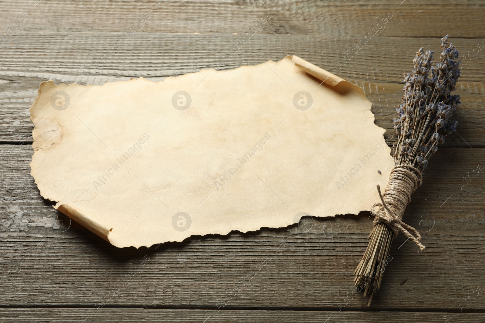 Photo of Sheet of old parchment paper and lavender flowers on wooden table