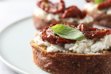 Photo of Delicious ricotta bruschetta with sun dried tomatoes and basil on plate, closeup